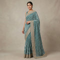 Woman wearing a teal saree with a beige border against a beige background