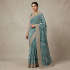 Woman wearing a teal saree with a beige border against a beige background