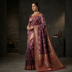 Woman wearing a purple and gold saree in a dimly lit room.