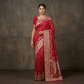 Woman wearing a red saree with gold patterns against a dark background