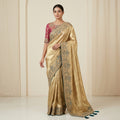 Woman wearing a gold saree with intricate patterns against a beige background