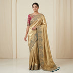 Woman wearing a gold saree with intricate patterns against a beige background