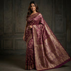 Woman wearing a purple saree with gold patterns against a dark background