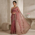 Woman wearing a pink saree with gold embroidery in an elegant indoor setting.